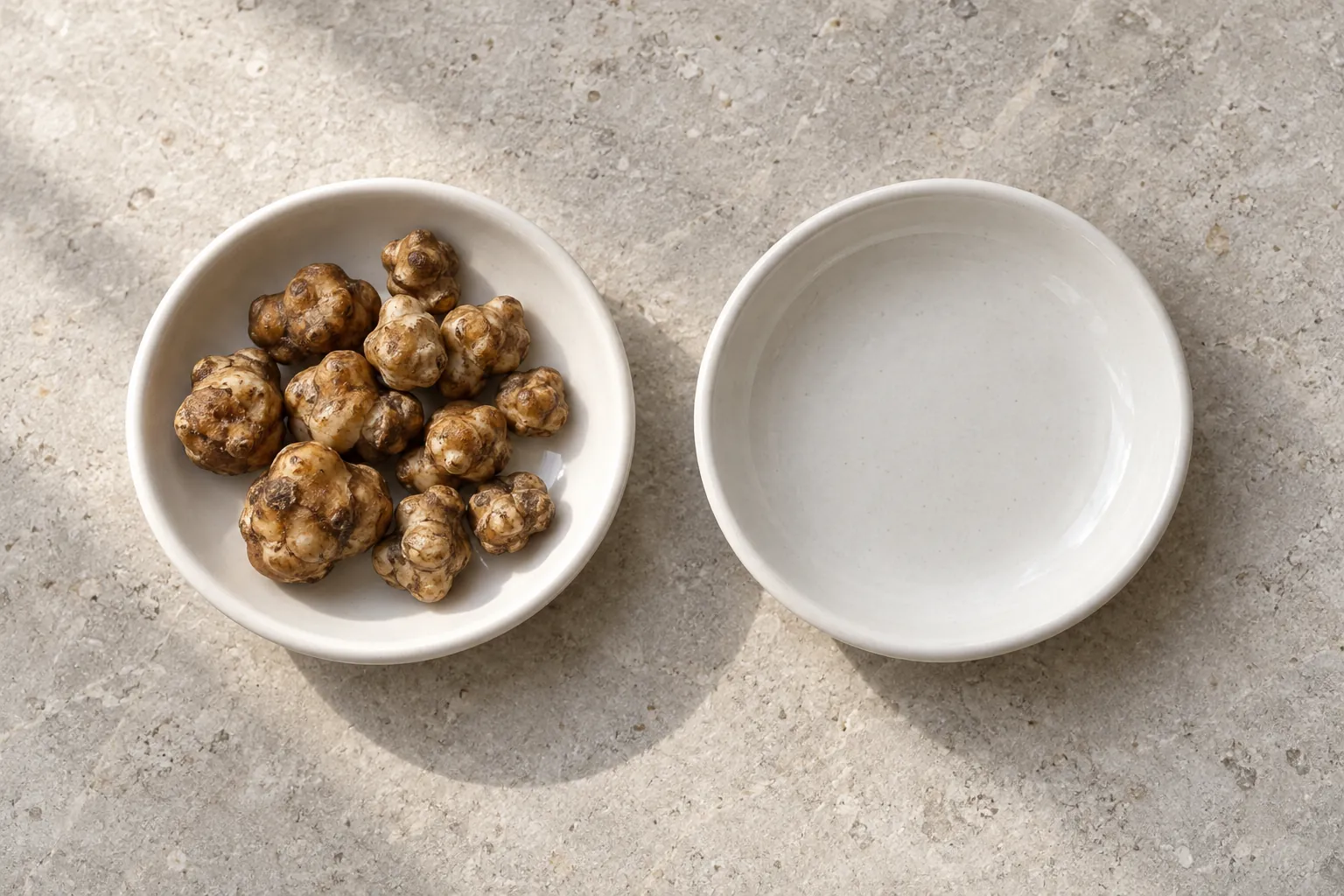 Dos cuencos blancos sobre piedra clara: uno con trufas frescas y otro vacío